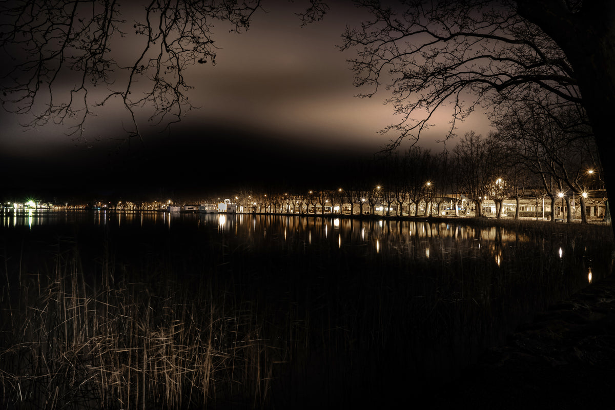 Paseo arbolado y farolas reflejados en el lago de Banyoles de noche. Fotografía fine art, edición limitada de 5 ejemplares.