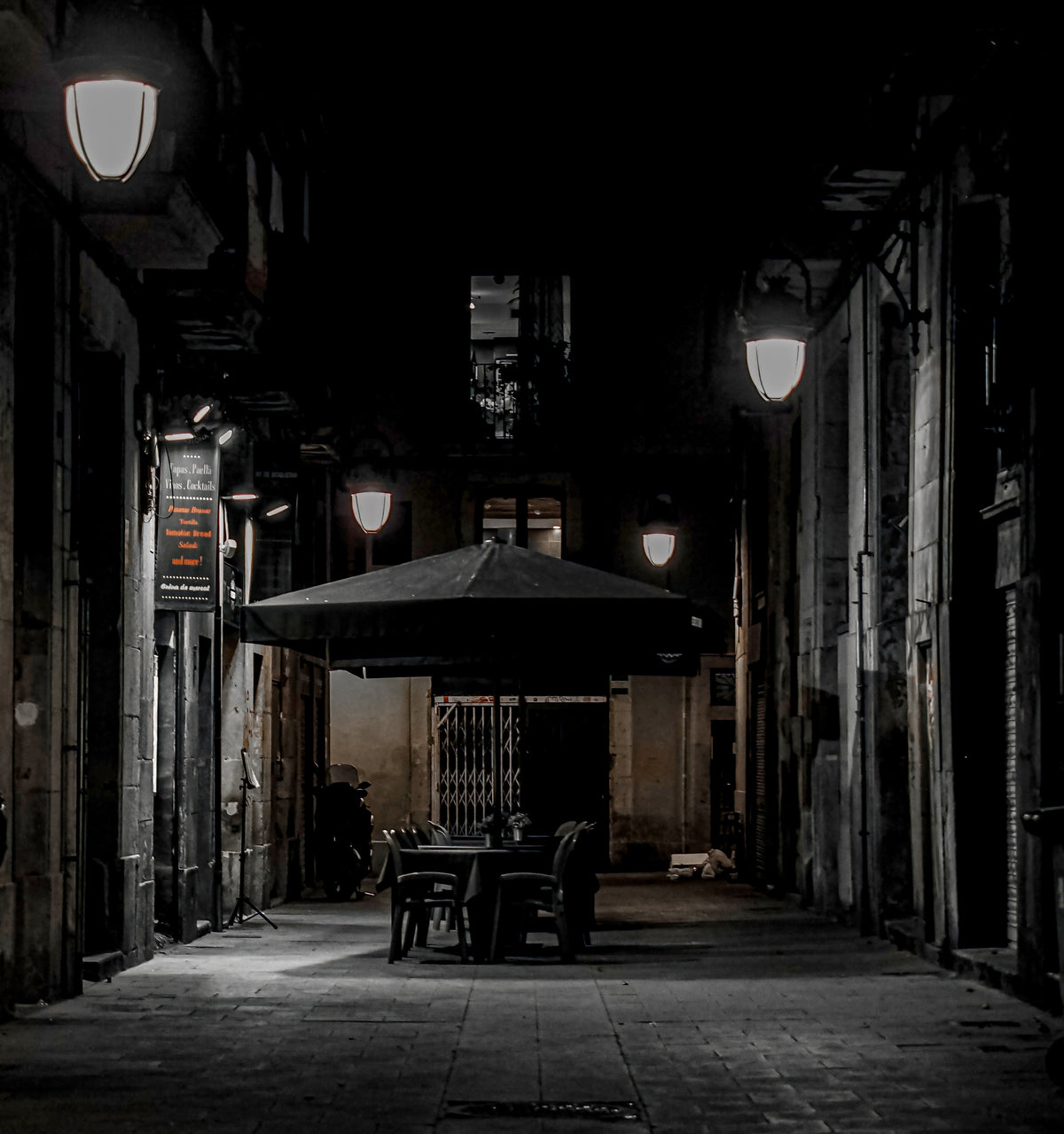 Empty terrace in a night alley of the Gothic Quarter, in black and white. Fine art photograph, limited edition of 5 copies.