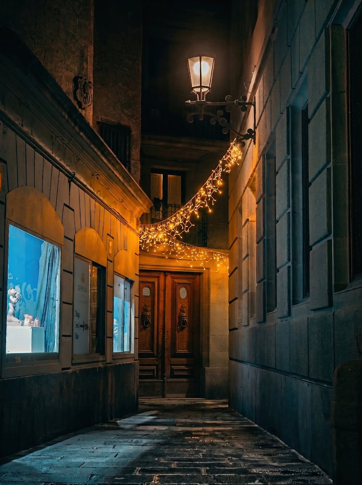Alley in the Gothic Quarter with a string of lights and a wooden door. Fine art photograph, limited edition of 5 copies.